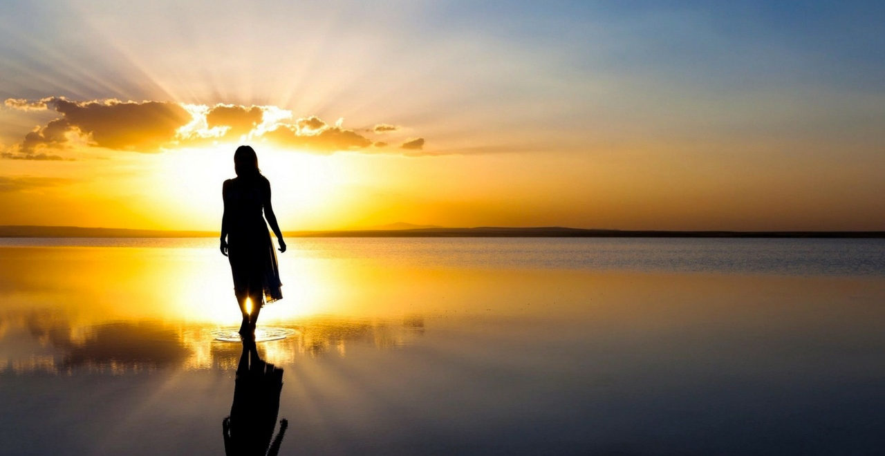 woman silhouette walking into calm water golden light